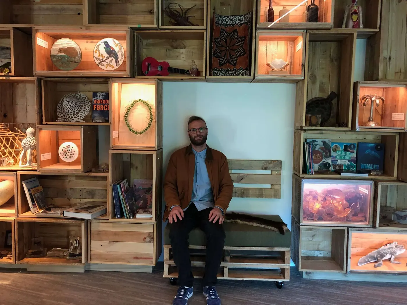 Dan Oakley sitting in front of a recycled crate display wall he built