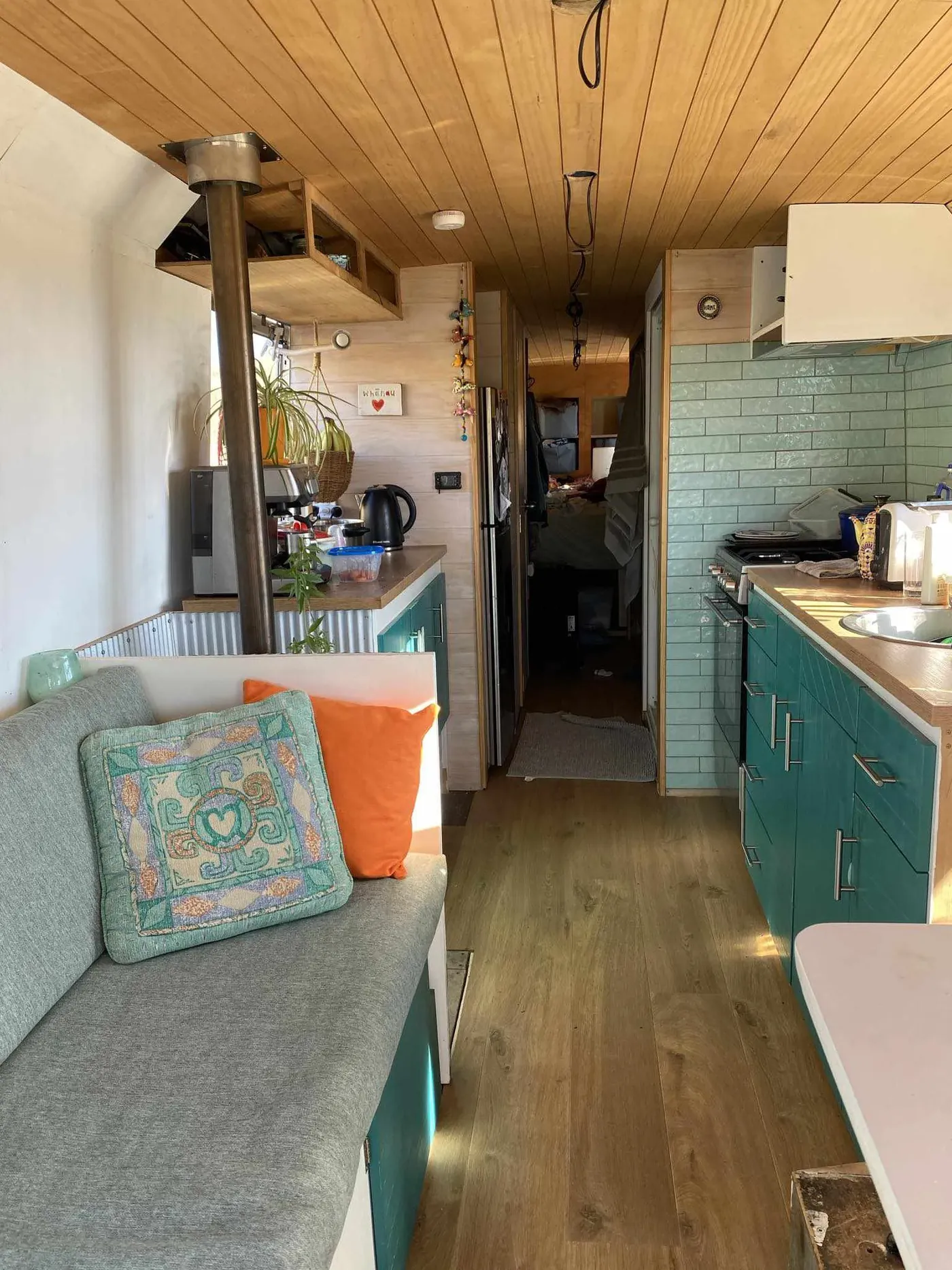 Finished tiny home interior with teal kitchen cabinetry and timber ceiling